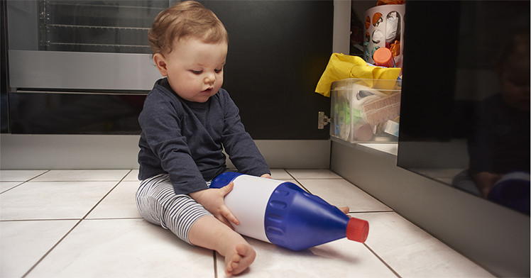 a baby on the kitchen floor playing with a bottle of household cleaner
